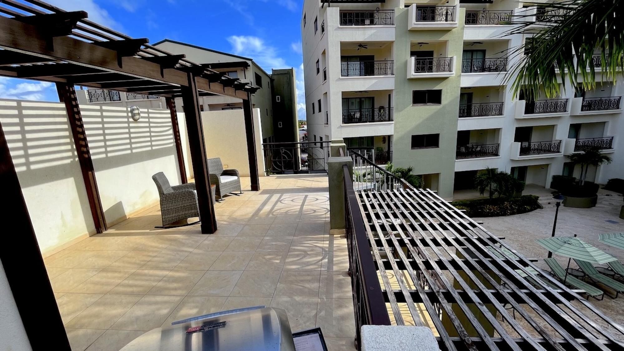 A rooftop patio with outdoor seating, a pergola, and a view of a multi-story building with balconies.