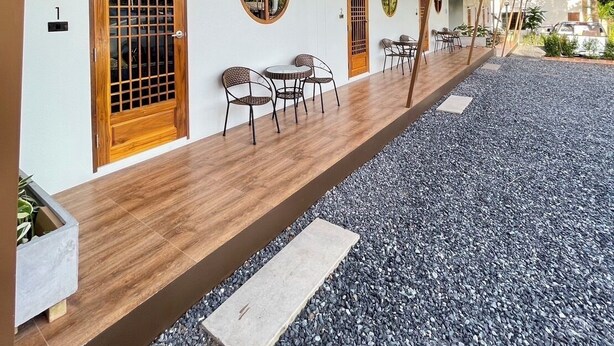 A building with a covered outdoor seating area, wooden doors, and a gravel ground. - Norn Na Homestay Chanthaburi (Chanthaburi)