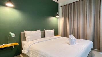 Una cama bien hecha con sábanas blancas, una mesita de noche con lámpara y una pared de acento verde.