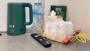 A green coffee maker, a water bottle, a remote control, a basket with toiletries, and a green card on a countertop. - Norn Na Homestay Chanthaburi (Chanthaburi)