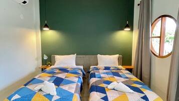 Quarto duplo com duas camas, uma parede verde de destaque e uma janela redonda.