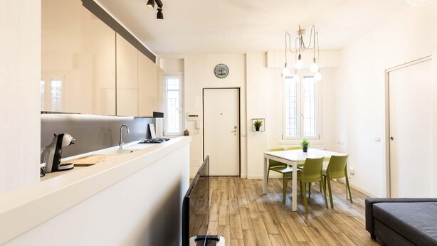 A modern kitchen with a built-in stove and sink, a dining area with a table and chairs, and a living area with a sofa. - Bellarmino 21 in Milano (Milan)