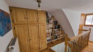 Un escalier en bois avec une rampe, menant à une mezzanine aménagée avec des étagères et un radiateur.
