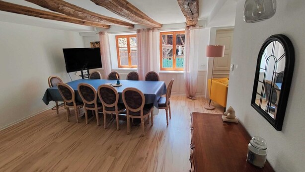 Un coin repas avec une table et des chaises en bois, un téléviseur et une fenêtre avec des rideaux.
