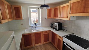 Une cuisine avec des meubles en bois, un plan de travail blanc, un évier, une cuisinière et une fenêtre donnant sur l’extérieur.