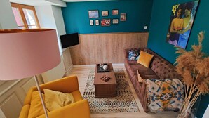 Un salon avec un mur d’accent de couleur turquoise, un canapé marron, un fauteuil jaune, une table basse et un téléviseur fixé au mur.