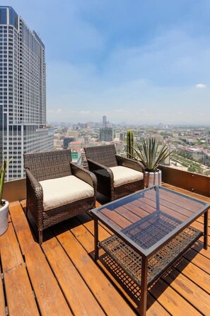 A wooden deck with wicker furniture and a glass table, overlooking a cityscape with tall buildings. - Unique panoramic terrace @ stunning 24 story tower (Ciudad de México)