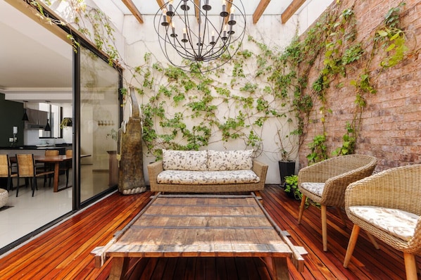 Eine gemütliche Terrasse mit einer Holzbank, Korbstühlen und einer gepolsterten Couch.