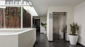 Ein modernes Interieur mit einer Rezeption, einem Holzzaun mit Bepflanzung, einer großen Topfpflanze und einem metallenen Aufzug.