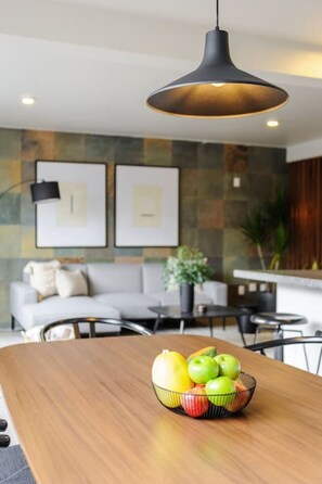 A modern living room with a wooden dining table, a bowl of fruit, a sofa, and a hanging pendant light. - Stylish 2-Bdr haven in the heart of Roma Norte (Ciudad de México)