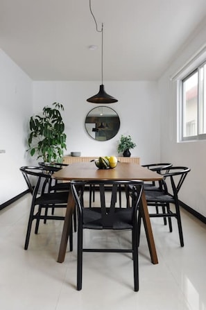 A dining area with a round table, black chairs, a hanging pendant light, and two potted plants. - Stylish 2-Bdr haven in the heart of Roma Norte (Ciudad de México)