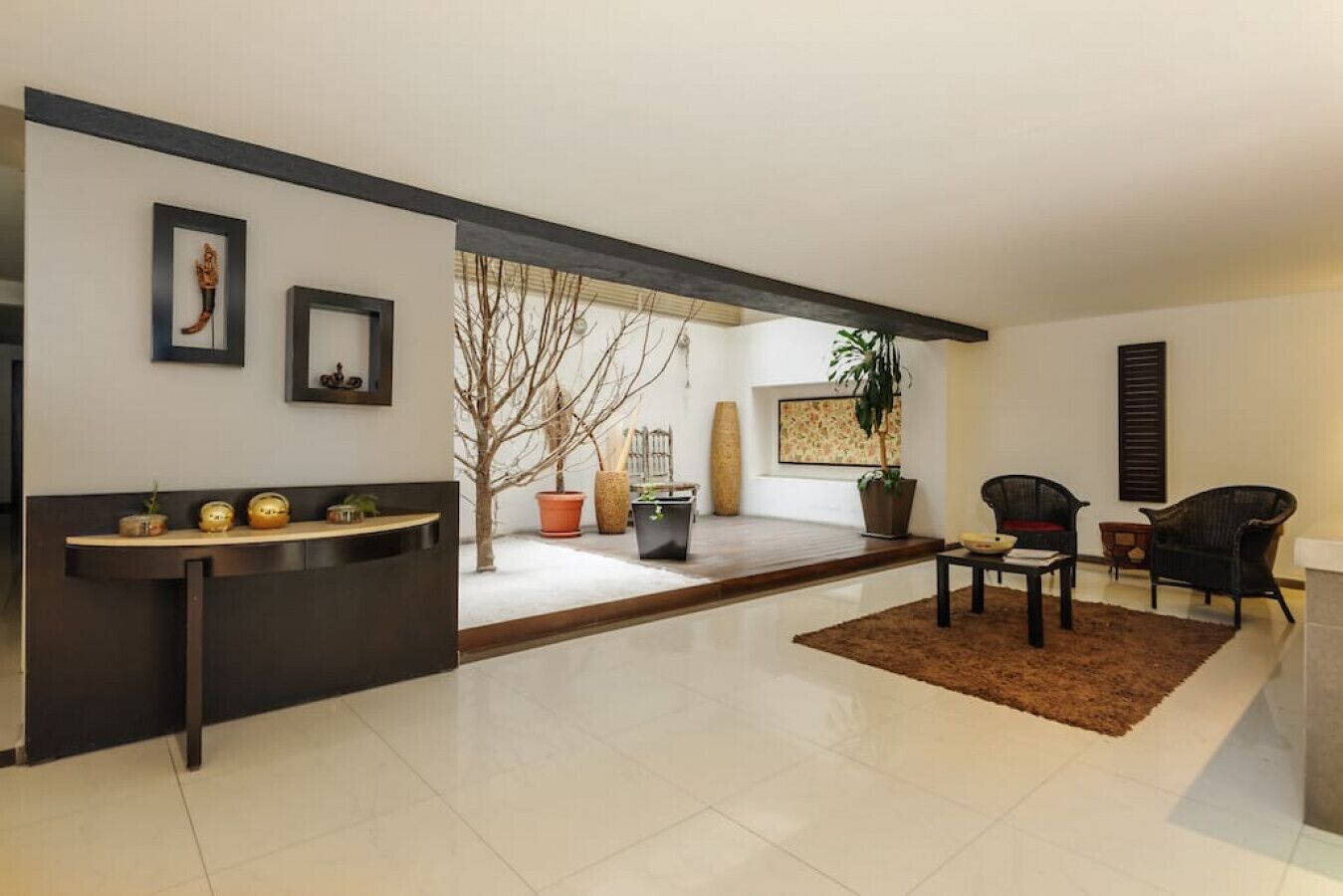 A modern living room with a dark reception desk, a coffee table, two armchairs, and a large potted plant.
