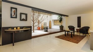 A modern living room with a dark reception desk, a coffee table, two armchairs, and a large potted plant. - Stylish 2-Bdr haven in the heart of Roma Norte (Ciudad de México)