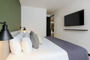 A modern hotel room with a bed, a mounted TV, and a lamp. - Stylish 2-Bdr haven in the heart of Roma Norte (Ciudad de México)