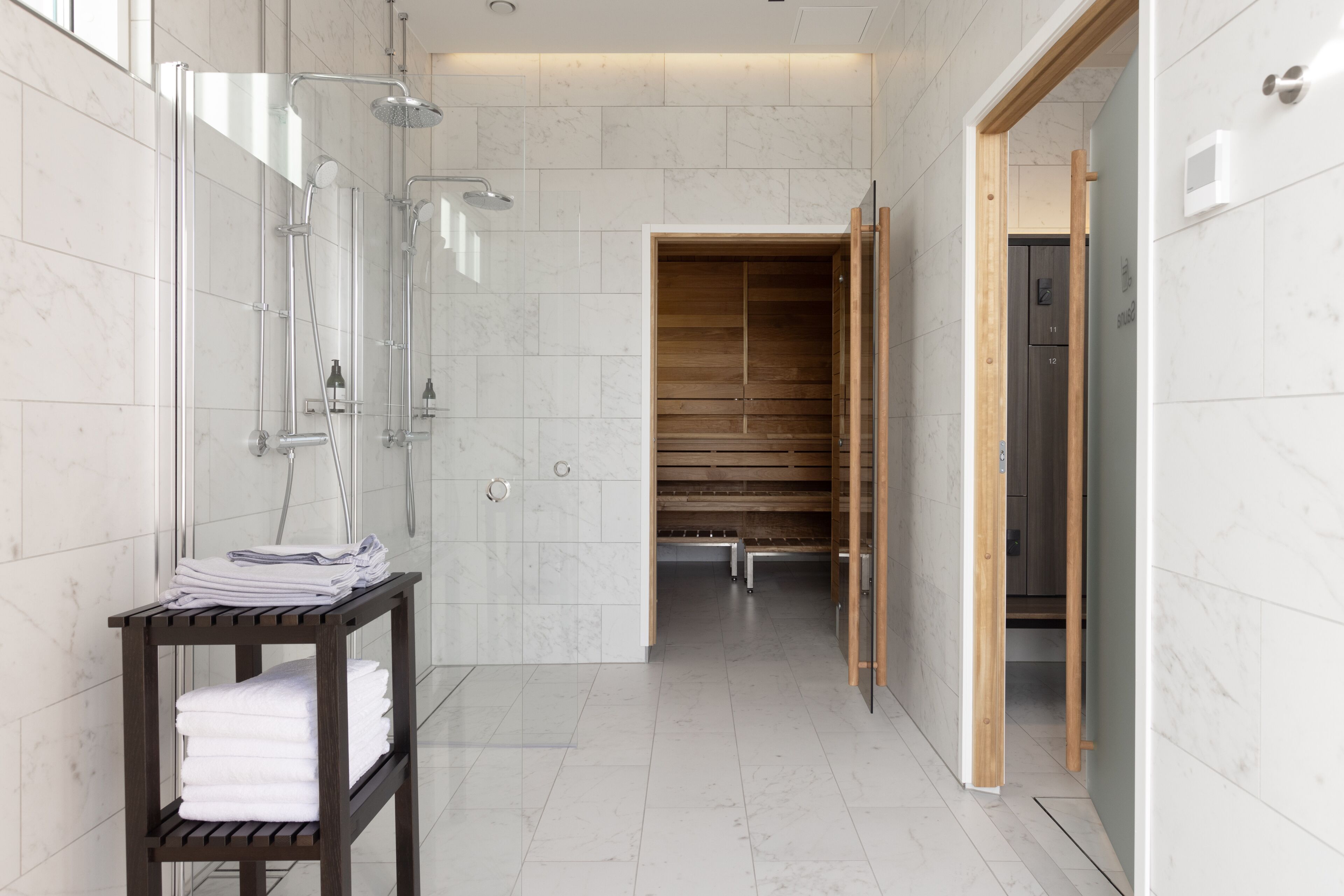 A modern bathroom with a glass shower enclosure, a wooden bench, and a towel rack.