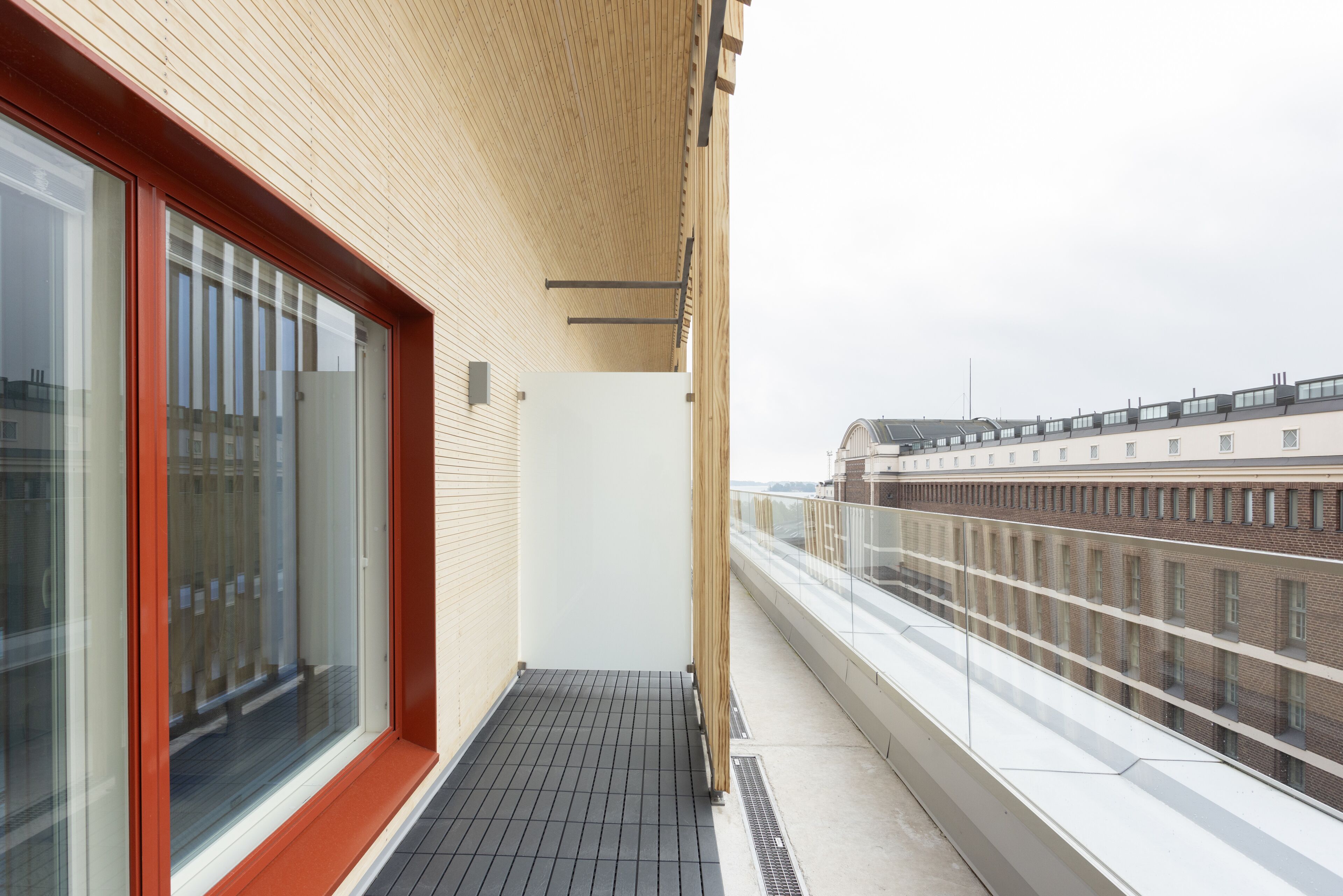 A balcony with a wooden ceiling, a glass door, and a view of a building with multiple windows.