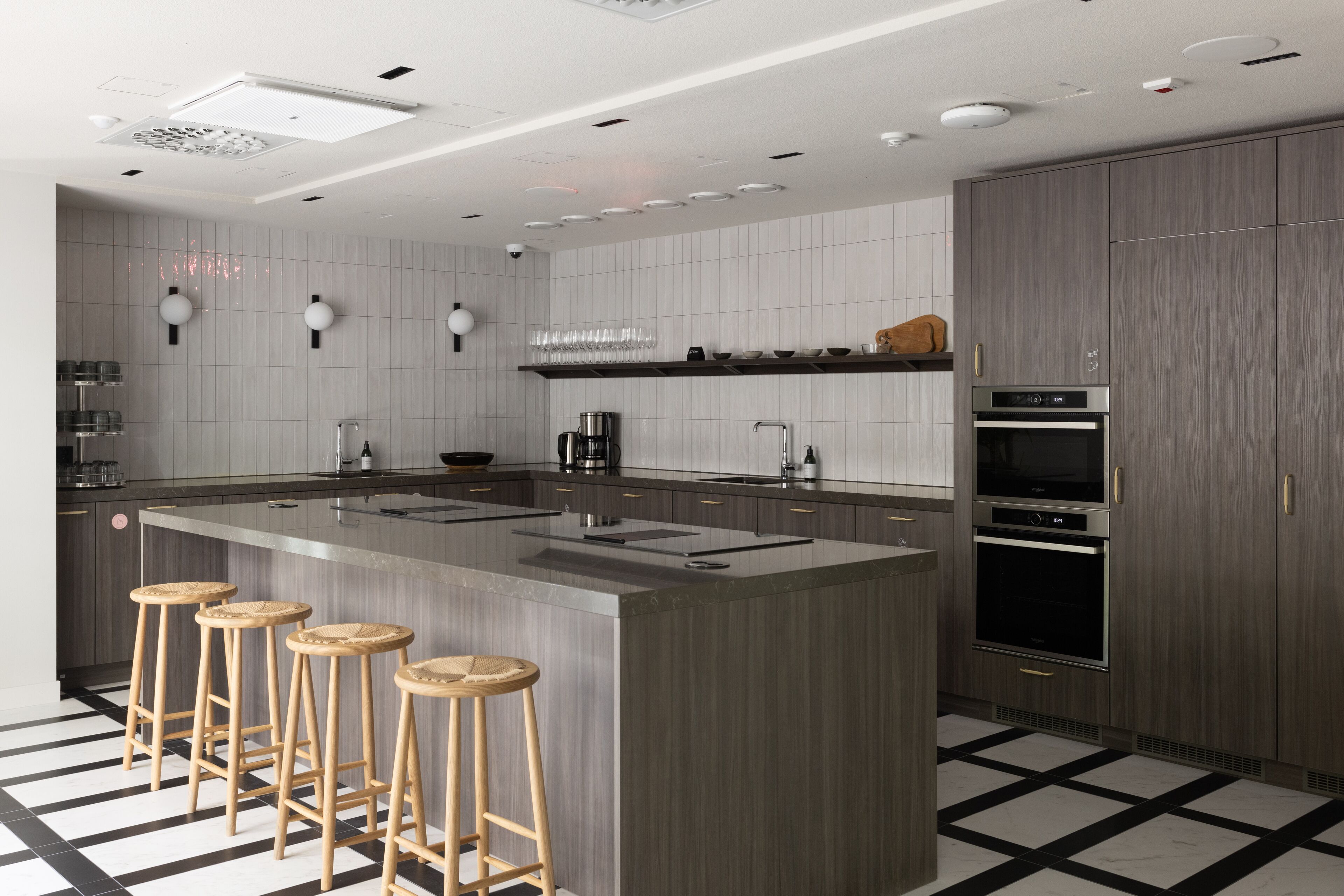 A modern kitchen with a large island, bar stools, stainless steel appliances, and a checkered floor.