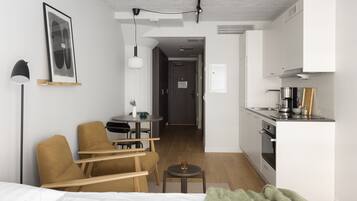 Habitación de hotel compacta con cama, sofá, una pequeña mesa, escritorio y kitchenette.
