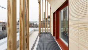 Ein Holzbalkon mit schwarzem Fliesenboden, einer roten Tür und Blick auf die Stadtlandschaft.