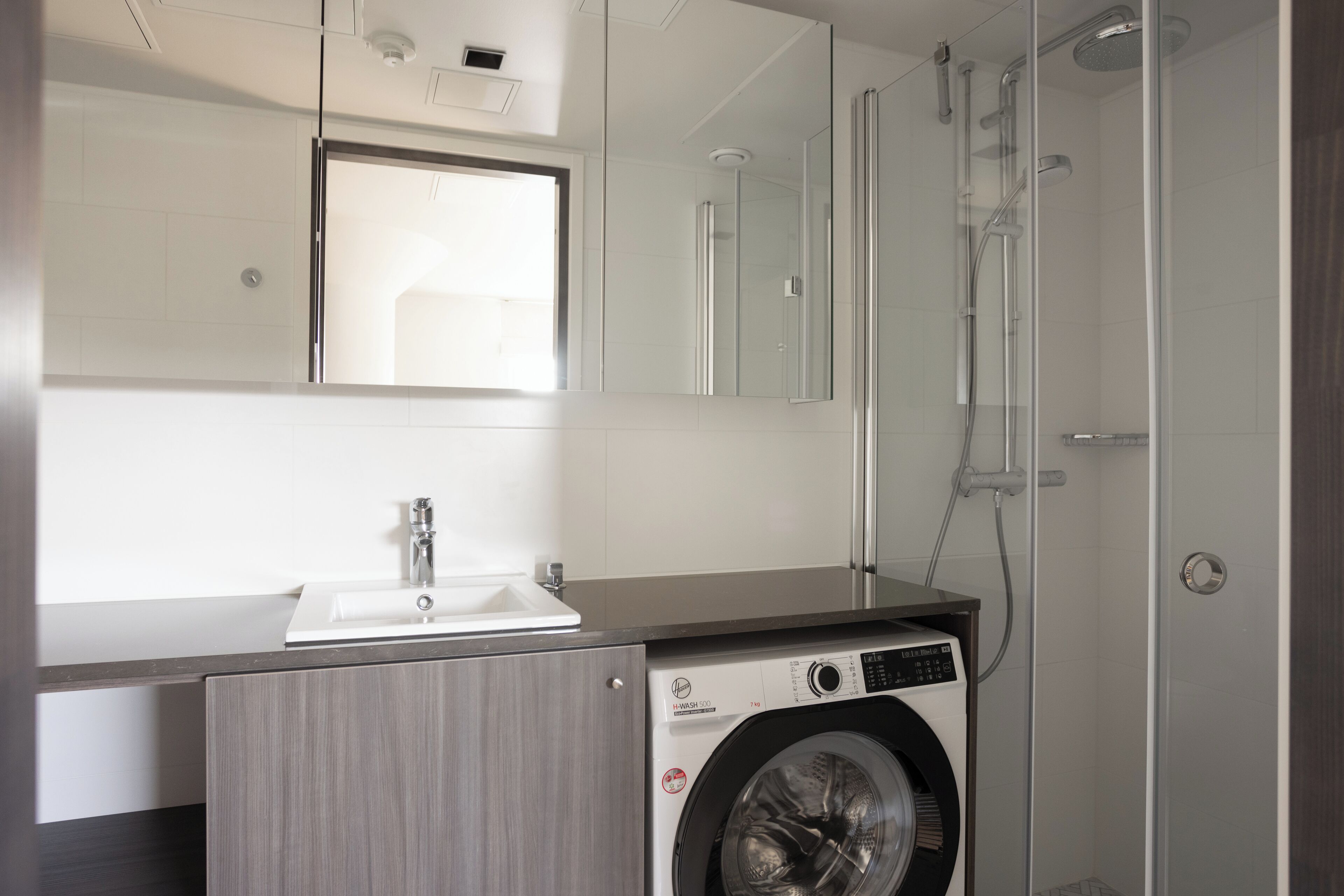 Ein modernes Badezimmer mit Waschmaschine, Waschbecken und einer Duschkabine aus Glas.