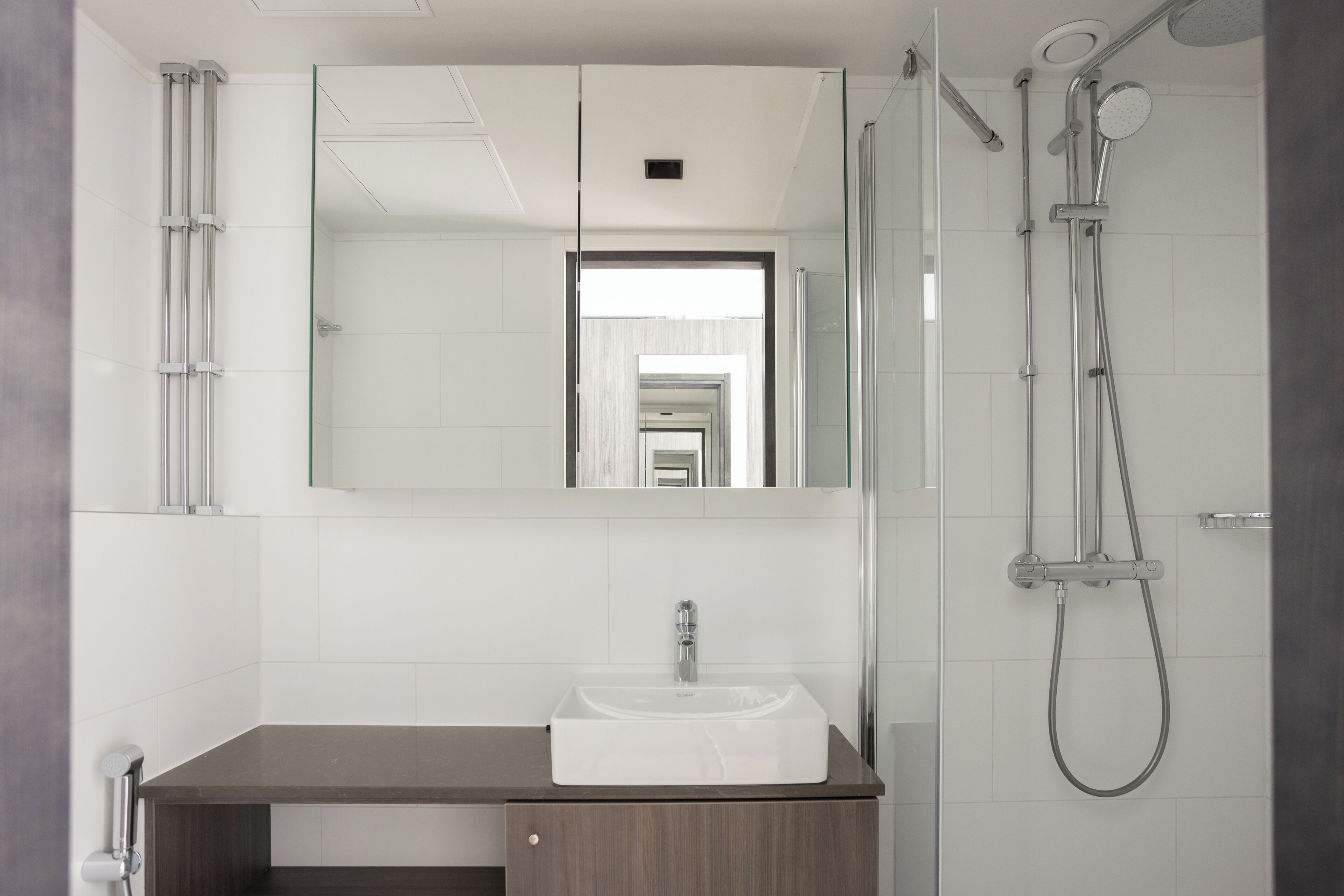 A modern bathroom with a white sink, dark countertop, and a glass shower enclosure.