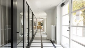 Ein Korridor mit Glastüren, Fliesenboden und Blick auf einen Speisesaal mit Tischen und Stühlen.