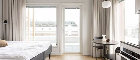 Habitación de hotel con cama, mesa de comedor con sillas, una pequeña cocina y vistas a través de puertas correderas.