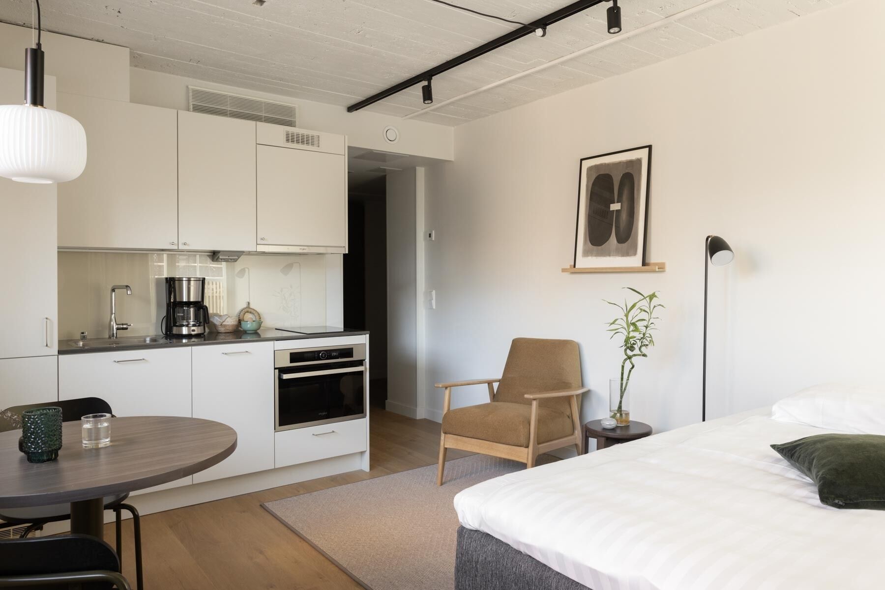 Une chambre d’hôtel de taille réduite, équipée d’une kitchenette, d’un lit, d’une chaise et d’une table de chevet.