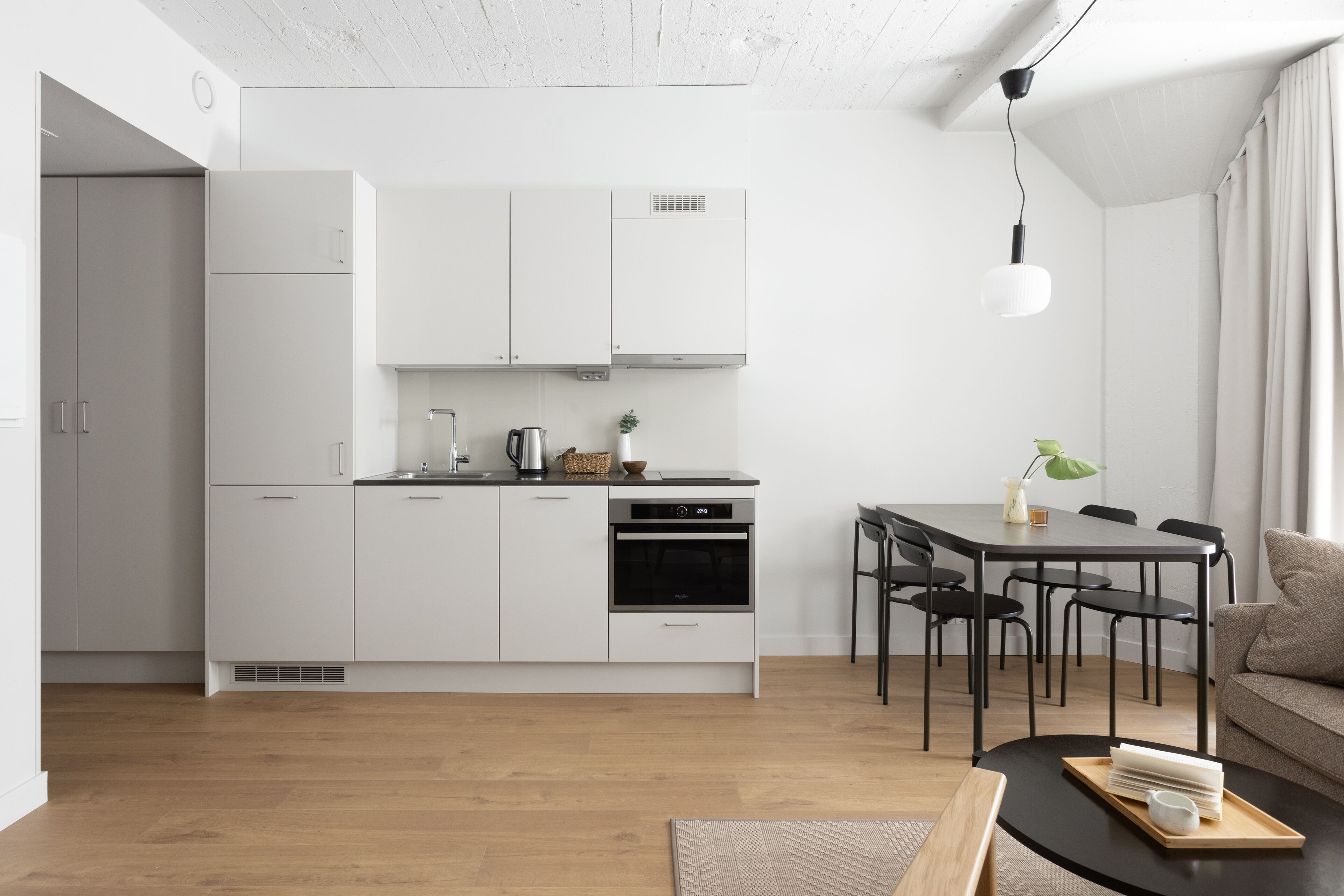 A modern kitchen with white cabinets, a dining area with a black table and chairs, and a wooden floor.