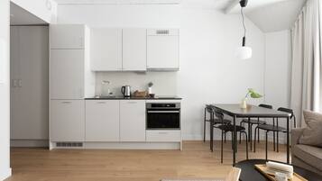 A modern kitchen with white cabinets, a dining area with a black table and chairs, and a wooden floor.