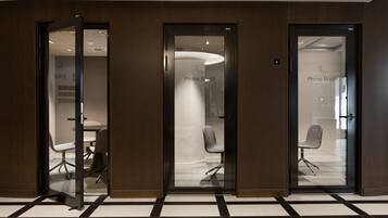 Un espace de bureau moderne doté de portes en verre portant l’inscription « Cabine téléphonique » et d’une salle de conférence avec une table et des chaises blanches.