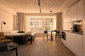 A compact hotel room with a bed, a desk with a laptop, a suitcase, a dining area, and a kitchenette. - Noli Katajanokka II (Helsinki)