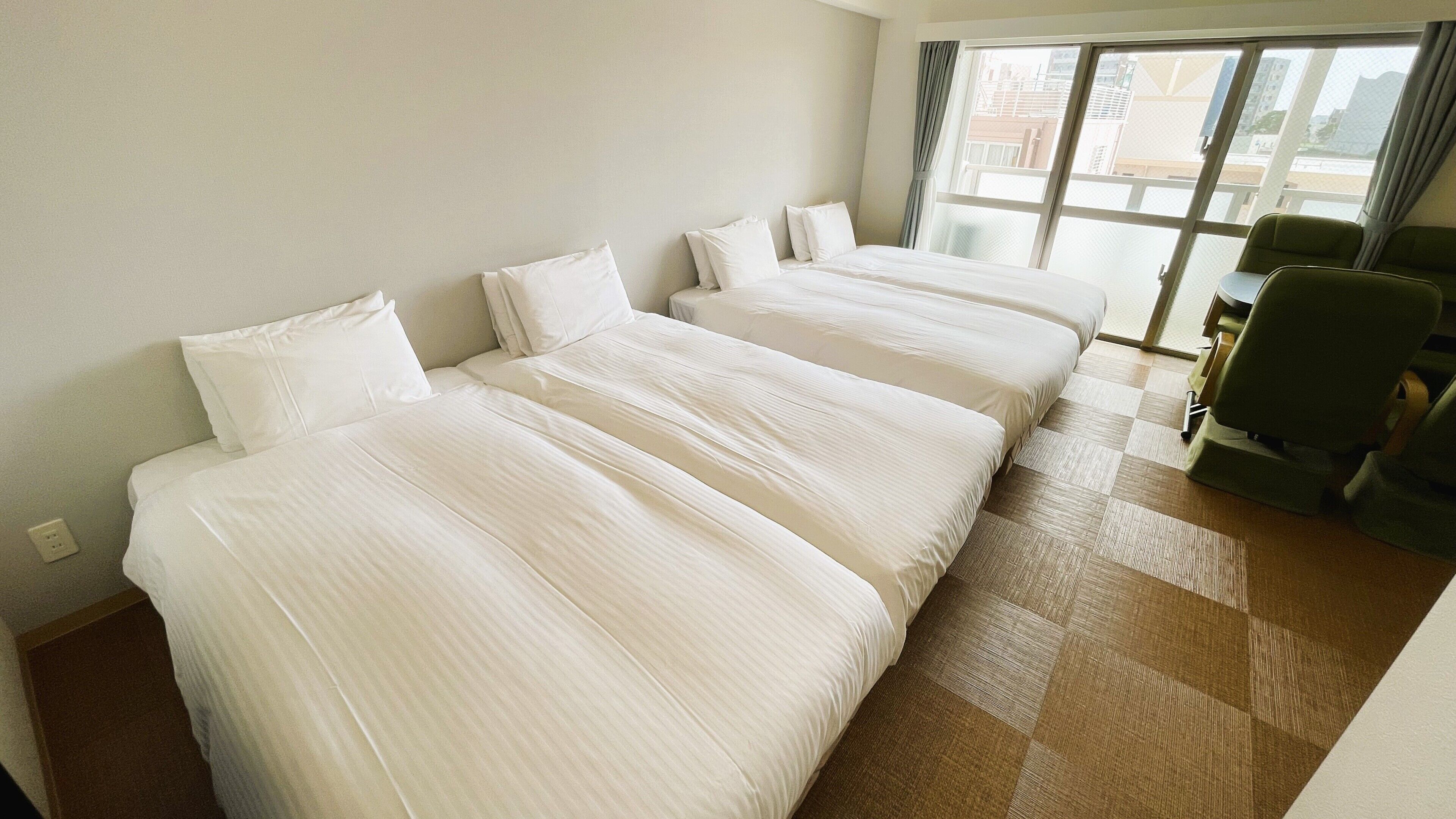 A hotel room with three beds, a window with curtains, a desk with a chair, and a check-in counter.