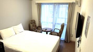 Una habitación de hotel con una cama grande, dos sillas, una mesita y un televisor.