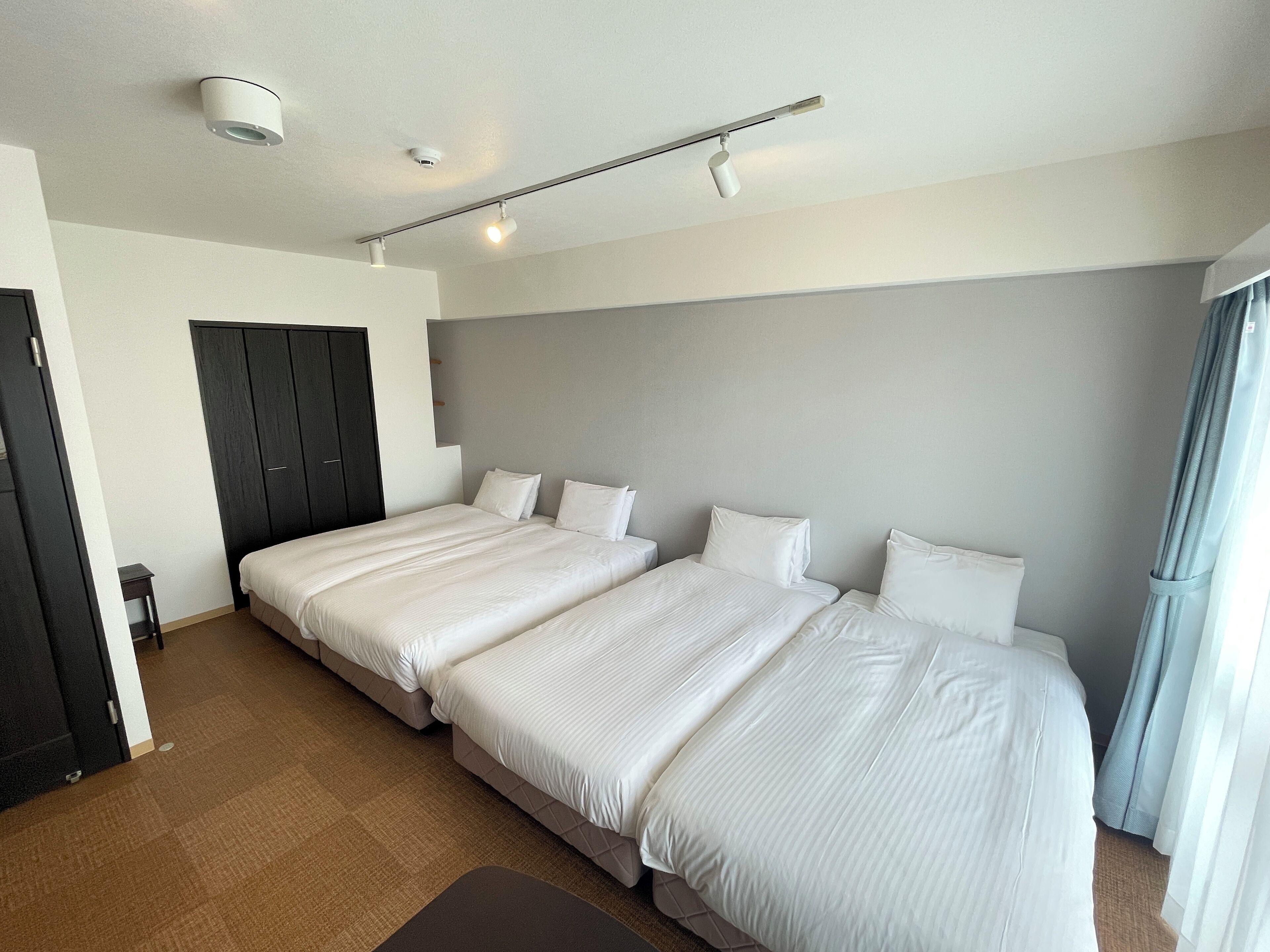 Habitación de hotel con dos camas, un armario oscuro, una mesita pequeña y una lámpara en el techo.
