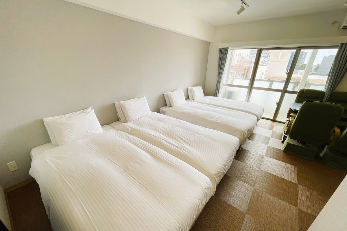 Quarto de hotel com três camas, uma mesinha e uma cadeira.