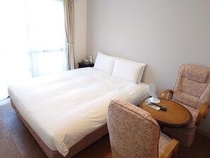 A hotel room with a large bed, a bedside table with a remote control, a chair, and a window with curtains. - BiBi Hotel Cosmos Shintoshin (Naha)