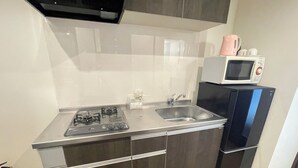 A compact kitchen with a gas stove, stainless steel sink, and a microwave on a black refrigerator. - BiBi Hotel Cosmos Shintoshin (Naha)