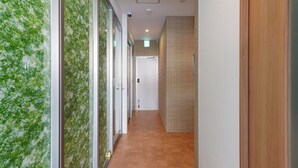 A hallway with a glass wall on one side, a wooden panel wall on the other, and a tiled floor. - BiBi Hotel Cosmos Shintoshin (Naha)