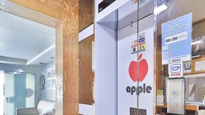 A modern hotel room with a bed, a bedside table, and a glass partition with an apple logo. - The Apple Hotel (Busan)