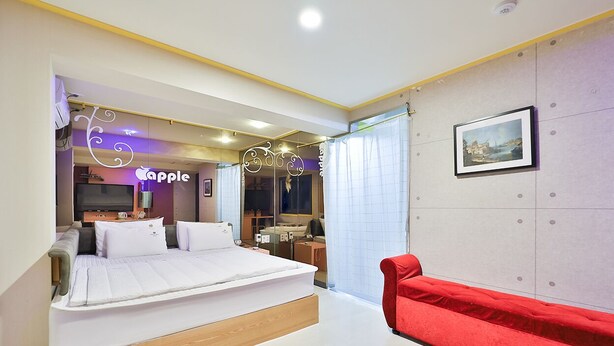 A modern bedroom with a bed, a red chair, a desk, and a neon sign. - The Apple Hotel (Busan)