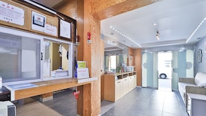 A modern hotel lobby with wooden accents, a reception desk, and a view of the street through glass doors. - The Apple Hotel (Busan)