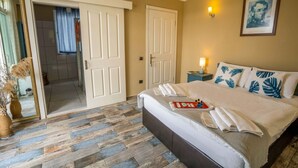 A hotel room with a large bed, a bedside table with a lamp, a mirror, and a door leading to another room. - Cunda Ada Kızı Otel (Ayvalik)