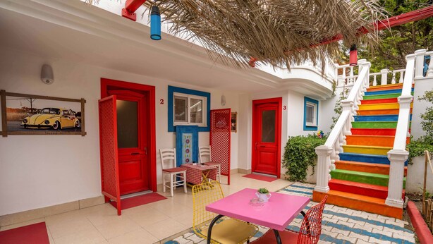 A colorful outdoor area with a staircase, a table with chairs, and a door with a red frame. - Cunda Ada Kızı Otel (Ayvalik)