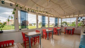A spacious dining area with large windows, red and blue chairs, and a wooden table. - Cunda Ada Kızı Otel (Ayvalik)