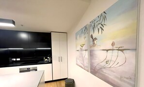 Una cocina moderna con armarios negros, encimera blanca y un cuadro con pájaros y flores en la pared.