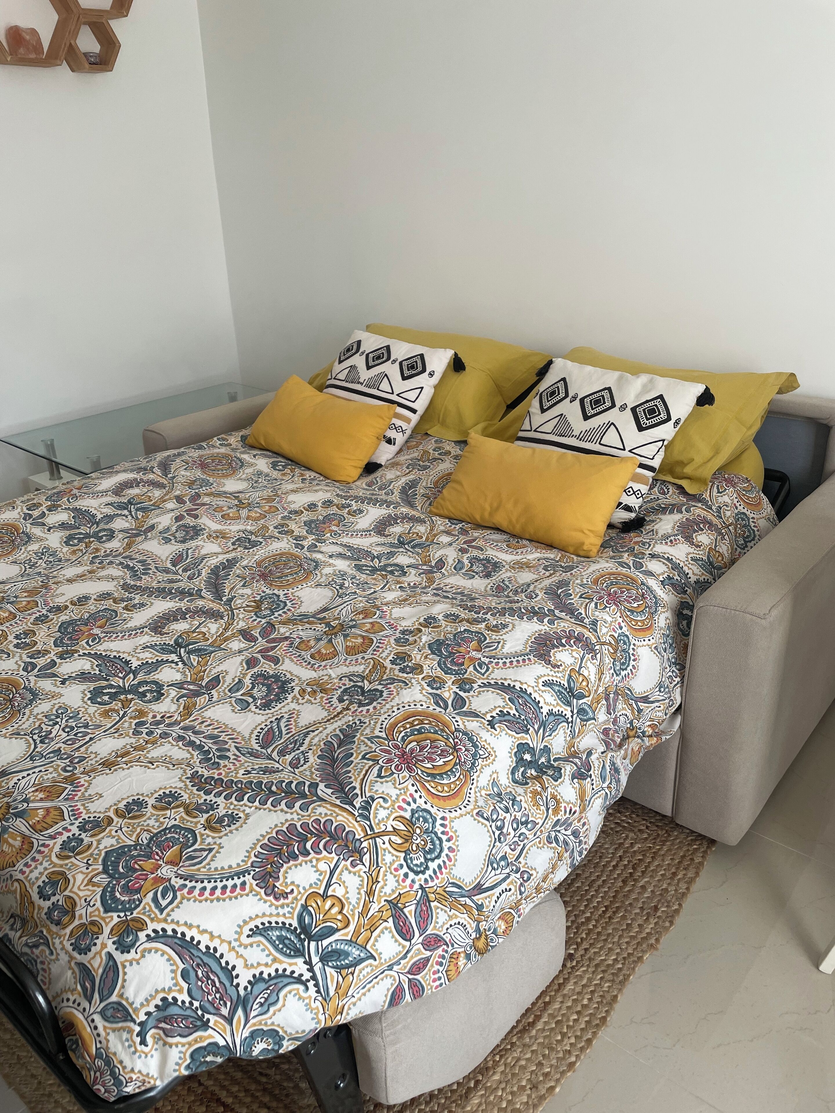 A bed with a patterned bedspread, multiple pillows, and a woven rug.