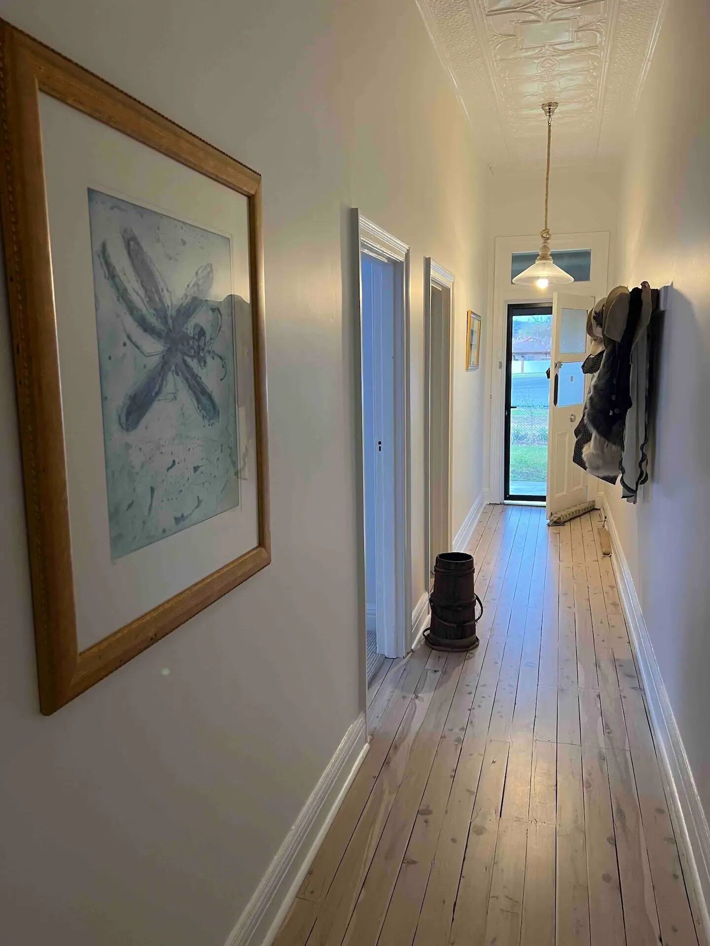 Un couloir doté d’un plancher en bois, d’un plafond orné de moulures décoratives et d’une porte donnant sur un espace extérieur.