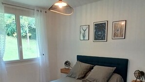 Un dormitorio con una cama, ventilador de techo, ventana con cortinas y tres cuadros en la pared.