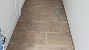 Un pasillo con suelo de madera, paredes blancas y una puerta al final.